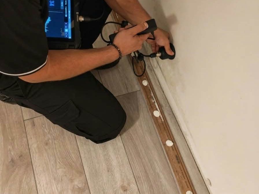 Mjerenje geofonom uz rub poda i zida, s nizom označenih mjernih točaka po liniji cijevi i prikazom zvuka na zaslonu uređaja