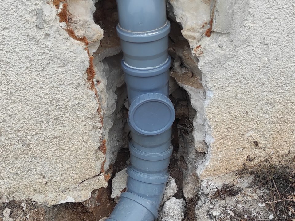 Prerađen pad odvodne cijevi Ø110 u otvorenoj niši fasade, s dva koljena od 45° na izlazu iz kuće, revizijom s okruglim poklopcem i blagim koljenima prema cesti, umjesto dva koljena od 90° na kojima se stvarao čep